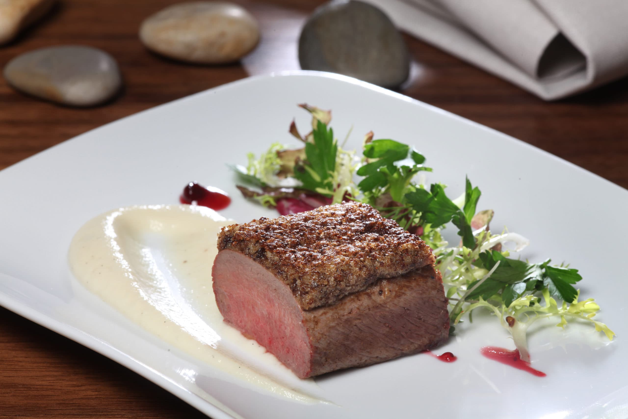 Rosa gebratenes Fleisch mit Kruste, heller Sauce und Salat