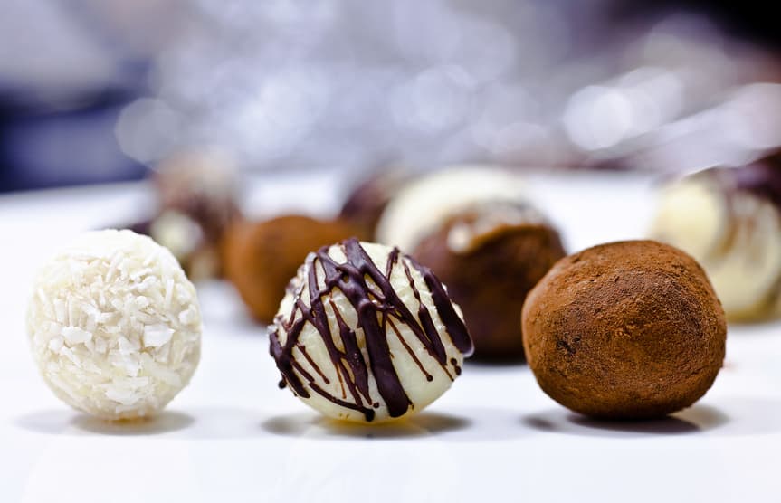 Pralinen mit Kokosraspeln, Schokoladenfäden und Kakao auf weißer Fläche